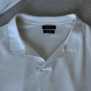 Vit pikétröja från Massimo Dutti - Snygg vit pikétröja från Massimo Dutti med klassisk krage och korta ärmar. Tröjan är tillverkad i fint tunt bomull och har en stilren, enkel design som passar perfekt till vår och sommar. Ribbad nederkant ger en schysst passform. Endast använd ett fåtal gånger! Jättefint skick!! Nypris 800kr