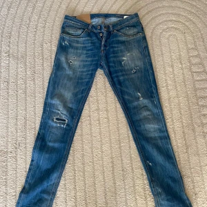 Dondup - Snygga blå skinny jeans från Dondup (modell George) med slitna detaljer och lätt tvättad look. Jeansen har klassisk femficksdesign, orange sömmar och skinny fit som sitter tajt längs benen. Perfekta för dig som gillar en modern och avslappnad stil. Storlek 31🌟