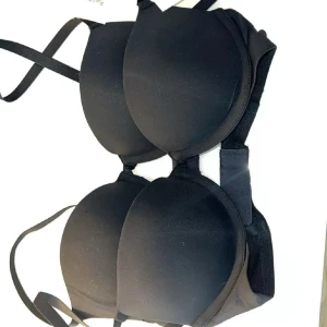 Svart axelbandslös bandeau-bh - Säljer en svart axelbandslös bandeau-bh med vadderade kupor och justerbara axelband. Bh:n har en slät och enkel design med hakknäppning bak. Perfekt under toppar och klänningar där du vill ha en osynlig look.