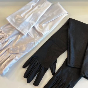 Långa svarta och vita satinhandskar - Två par eleganta, långa handskar. Använda fåtal gånger och har några synliga tecken på användning men inget men tänker på. 