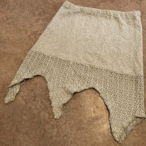 Grå stickad kjol med spetskant - Unik grå stickad kjol med asymmetrisk spetskant nertill. Kjolen har en cool, ojämn nederdel som ger en edgy vibe och är perfekt för dig som vill sticka ut. Mjuk och bekväm med snyggt mönstrad spetsdetalj längs hela kanten.