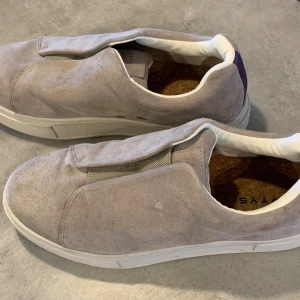 Grå mockasneakers från EYTYs - Snygga sneakers från EYTYs i ljusgrå mocka med vit sula och diskret elastisk detalj framtill. Skorna har en minimalistisk design, rund tå och bekväm innersula i kork. Perfekta för dig som gillar stilrena och cleana sneakers. Använda vid två tillfällen. Nypris 2200kr