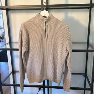Beige stickad half zip-tröja 157 - Beige stickad tröja från 157 med ribbad struktur och hög krage. Tröjan har en snygg half zip-dragkedja framtill och långa ärmar. Perfekt för lager-på-lager och chill höst- eller vinterstil.