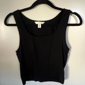 Svart linnetopp från H&M - En stilren svart linnetopp från H&M i klassisk modell med breda axelband och rundad halsringning. Toppen är ärmlös och tillverkad i mjuk bomull, perfekt att matcha med jeans eller kjol för en enkel och snygg look.