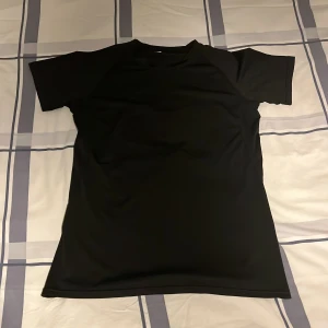 Svart t-shirt med vit ryggdesign - Svart t-shirt i syntetmaterial med korta ärmar och en unik vit grafisk design på ryggen som liknar vingar och ryggrad. Perfekt för dig som vill sticka ut med en edgy och cool look. Detta är då en gymtröja som är compressed i storlek s/m