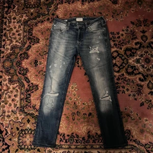 Jack & Jones slim Liam jeans blå 33/34  - Snygga blå skinny jeans från Jack & Jones, modell Liam. Jeansen har slitna detaljer och hål på benen för en cool, avslappnad look. Klassisk femficksmodell med dragkedjegylf och smal passform. Perfekta för dig som gillar streetstyle. Midja 37cm längd 90cm (57)