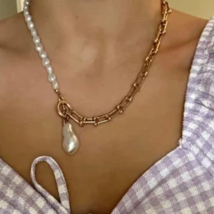 Halsband med pärlor och guldlänk - Unikt halsband med ena halvan i vita pärlor och andra halvan i guldfärgad kedja. Hängsmycke i oregelbunden pärlform ger en cool kontrast. Perfekt för dig som gillar att sticka ut med accessoarer.