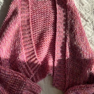 Rosa stickad kofta från Pull&Bear - Supermysig rosa stickad kofta från Pull&Bear i chunky garn med inslag av lila och orange. Koftan har bred ribbad kant, öppen framtill och långa ärmar. Perfekt för lager-på-lager och ger en färgklick till din outfit.