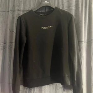 Svart sweatshirt från Armani Exchange - Svart sweatshirt från Armani Exchange med stilren logga i vitt på bröstet. Klassisk rund halsringning och långa ärmar. Tillverkad i mjuk bomullsmix som är skön att bära. Perfekt för en clean och enkel look.