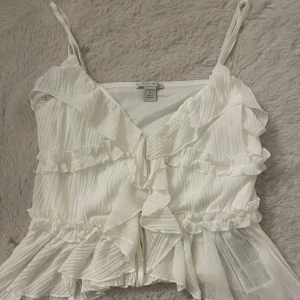 Vit volangig linnetopp från Amisu - Supersöt vit linnetopp från Amisu med tunna axelband, volanger och knyt framtill.  Toppen är i storlek M och säljer pågrund av att den var för stor, prislappen finns kvar och är som ny! 