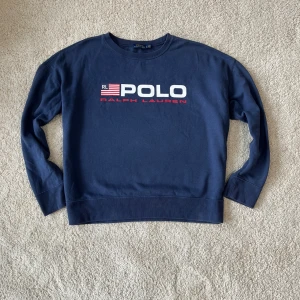 Ralph Lauren USA Tröja - Snygg blä sweatshirt frän Ralph Lauren med stort USA tryck pà framsidan. Tröjan har rund hals och länga ärmar, perfekt för vintern och den är i toppskick! Storlek: LG/ 165-175. Kom med bud!