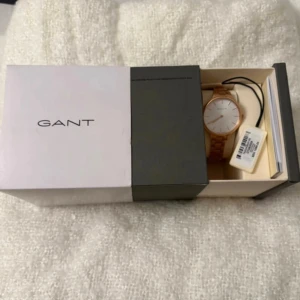 Guldigt armbandsur från GANT - Snygg klocka från GANT med guldigt metallarmband och vit urtavla. Stilren design med minimalistiska detaljer och klassisk rund form. Perfekt accessoar för dig som gillar en clean look och vill ha något som sticker ut lite extra.