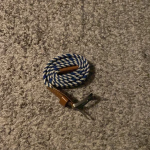 Randigt blåvitt bälte med skinn - Säljer ett snyggt flätat bälte med randigt mönster i blått och vitt. Bältet har detaljer i brunt skinn vid ändarna och ett klassiskt metallspänne. Perfekt accessoar för att lyfta din outfit med lite färg och stil.