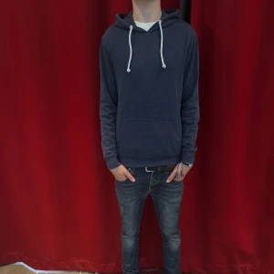 Mörkblå hoodie med huva och snörning - Säljer en mörkblå hoodie med vit snörning och stor ficka framtill. Tröjan har en klassisk huva och är långärmad, perfekt för chill dagar. Passar dig som gillar enkel och stilren streetwear.