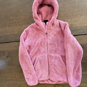 Rosa teddyjacka med huva från Everest - Mysig rosa teddyjacka från Everest med huva och dragkedja framtill. Jackan har två stora fickor och är tillverkad i fluffigt teddy-material som håller dig varm. Perfekt för kyliga dagar och enkel att matcha med dina favoritjeans eller mjukisbyxor.