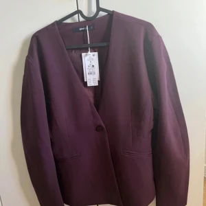 Vinröd kavaj från Gina Tricot - Snygg vinröd kavaj från Gina Tricot i storlek S. Modellen har en skulpterad passform med v-ringad hals och en knapp framtill. Kavajen är tillverkad i ett slätt material och har två fickor framtill. Nypris: 699 kr