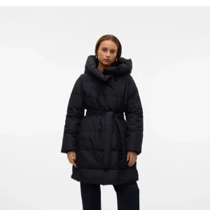 Svart pufferjacka från Vero Moda  - Säljer en svart pufferjacka från Vero Moda i storlek M. Jackan har huva, knappar och bälte i midjan för extra snygg passform. Perfekt för kalla dagar när du vill hålla dig varm och ändå se stilren ut.