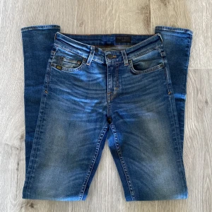 Blå jeans från Tiger of Sweden - Snygga blå jeans från Tiger of Sweden med klassisk femficksdesign och bruna detaljer på bakfickan. Jeansen är slim fit och är tillverkade i slitstarkt denimtyg med snygg tvätt och kontrastsömmar. Byxorna är i W27 men passar mer W28 och W29
