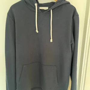 Mörkblå hoodie från Pier One - Säljer en stilren mörkblå hoodie från Pier One med vit snörning i huvan och klassisk känguruficka framtill. Tröjan har långa ärmar och en skön passform, perfekt för chill dagar. Materialet är mjuk bomull som känns bekvämt mot huden.