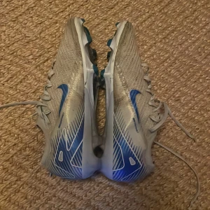 Vapor 16 elite  - Nypris 3600 mitt pris 1299. Skicket är bra men inte i nyskick men fungerar helt perfekt. Säljer ett par Nike fotbollsskor i silver med blå detaljer och snörning. Skorna har en sportig design med mönstrad ovandel och dobbar för bra grepp på planen. Perfekta för dig som vill sticka ut med stil på matchen.