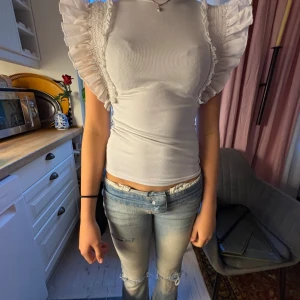 Vit blus med volangärmar - Supersöt vit blus med stora volangärmar och smockdetaljer på axlarna. Toppen är figurnära och har en rund halsringning. Perfekt för dig som vill ha en feminin och trendig look med extra statement på axlarna. 😻😻😻