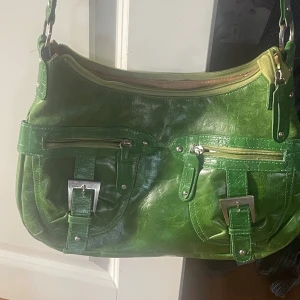 Grön axelväska från The Monte - Cool grön axelväska i skinn från The Monte med två framfickor med spännen och dragkedjor. Insidan är fodrad med brunt tyg och har flera fack för småsaker. Perfekt storlek för att få plats med allt du behöver och har snygga detaljer i silver.