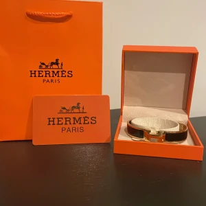 guldarmband med H-detalj  - Guldigt armband i svart och guld med ikoniskt H-spänne. Kommer i originalask och med äkthetskort. Hör av dig om du undrar något 