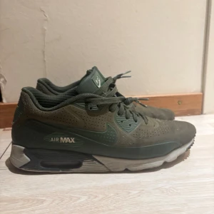 Nike Air Max sneakers i mörkgrönt - Säljer ett par Nike Air Max sneakers i mörkgrönt med perforerad ovandel och klassisk Air Max-dämpning i sulan. Skorna har snörning, rund tå och är tillverkade i syntetmaterial. Perfekta för dig som gillar streetwear och sportig stil.