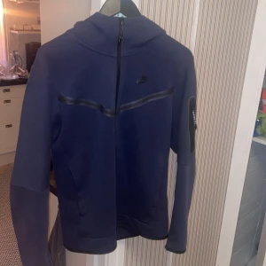 Mörkblå Nike hoodie med dragkedja - Nike tech  hoodie i mörkblått med hel dragkedja och huva i storlek S men passar M också, Mycket bra skick .