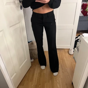 Svarta kostymbyxor med bootcut - Snygga svarta kostymbyxor med bootcut-snitt och låg midja. Byxorna har klassiska fickor fram och bak, samt hällor för bälte. Perfekt passform som ger en clean och stilren look. Materialet är mjukt och följsamt, troligtvis polyester eller bomullsmix.
