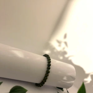 Grönt pärlarmband med rundade pärlor - Snyggt armband med små, rundade pärlor i mörkgrön färg. Perfekt för dig som gillar minimalistisk stil och vill ha något enkelt men ändå unikt på handleden. Passar både till jeans och hoodie eller när du vill addera lite färg till din outfit.