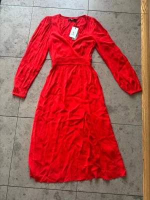 Röd omlottklänning från BikBok - Snygg röd omlottklänning från BikBok med långa puffärmar och markerad midja. Klänningen har v-ringning och är tillverkad i ett lätt, mjukt tyg som ger ett fint fall. Perfekt för dig som vill sticka ut med färg och stil.