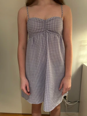 Ljuslila rutig sommarklänning - Söt ljuslila och vit rutig klänning med smala axelband och lätt rynkad byst. Klänningen är kort och har en avslappnad passform, perfekt för sommaren. 