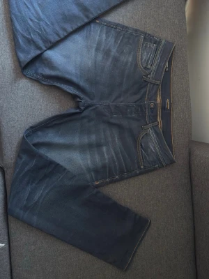 Mörkblå jeans från Jack & Jones - Säljer ett par mörkblå jeans från Jack & Jones med klassisk femficksdesign och snygga slitningar framtill. 32/32. Jeansen väldigt små skador på bakfickan men inget som syns (finns på bild)