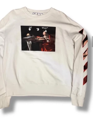 Vit sweatshirt från Off-White - Vit sweatshirt från Off-White med tryck av klassiskt konstmotiv på bröstet och röda diagonala ränder på ena ärmen. Rund halsringning och avslappnad passform. Tillverkad i mjuk bomull för maximal komfort. Perfekt för dig som gillar streetwear och unika prints.
