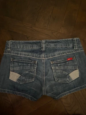 Blå jeansshorts från Only - Säljer ett par klassiska blå jeansshorts från Only med låg midja och fem fickor. Shortsen har slitna detaljer och kontrastsömmar, samt bälteshällor och knappstängning framtill. Perfekta för varma dagar och enkel att matcha. Skulle säga xs i storlek!