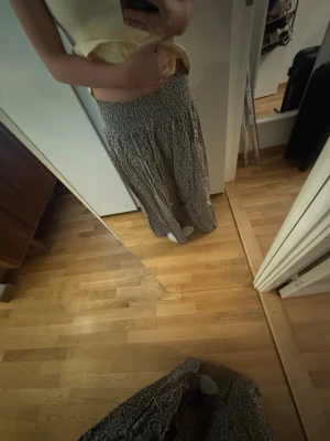 Mönstrad långkjol i svart och beige - Säljer en flowy långkjol med svart och beige mönster. Kjolen har ett bohemiskt, nästan paisley-liknande tryck och är gjord i ett lätt material som passar perfekt till varmare dagar. Resår i midjan för skön passform.