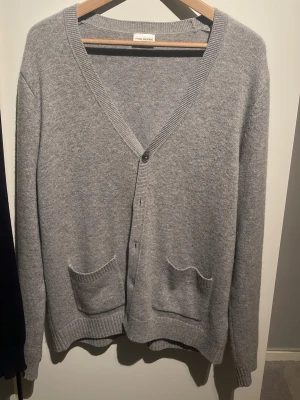 Grå kofta från John Henric - Klassisk grå kashmir kofta från John Henric med v-ringning och knäppning framtill. Två fickor fram och ribbade muddar vid ärmslut och nederkant. Perfekt för lager på lager och enkel att matcha med olika outfits. 10% kashmir