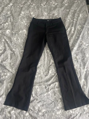 Lågmidjade kostymbyxor  - Svarta lågmidjade kostymbyxor med slits från BikBok i storlek 38. Modellen heter Vera. Nypris 500kr. Inga defekter! Vi kan komma överens om ett bra paketpris ifall du vill köpa flera varor!