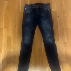 Mörkblå jeans från Replay - Säljer ett par mörkblå jeans från Replay med snygga slitningar och tvättade detaljer. Klassisk femficksmodell med smal passform och silverfärgade nitar. Perfekta för dig som gillar en modern och stilren look.