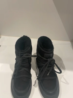Svarta vinterboots med snörning - Säljer ett par svarta vinterboots med högt skaft och kraftig snörning runt hela skon. Insidan är fodrad med mjukt material för extra värme. Yttermaterialet är en mix av mocka och textil. Använda få gånger och säljer för de är för små. På ena skon är fästet där bak sönder men de funkar utmärkt ändå!!