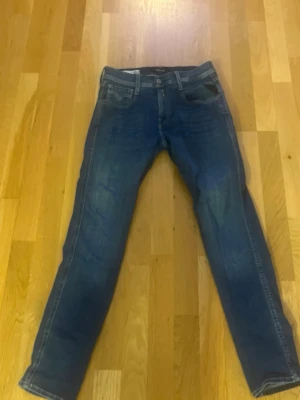 Blå jeans från Replay - Säljer ett par klassiska blå jeans från Replay med raka ben och femficksmodell. Jeansen har snygga slitningar och kontrastsömmar samt Replay broderad på bakfickan. Tillverkade i slitstark denim, perfekta för en avslappnad stil.