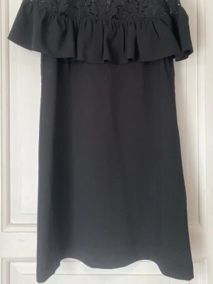 Svart kort klänning med spets och volang - Supersnygg svart klänning från H&M med spets upptill och volangdetalj över axlarna. Klänningen är ärmlös och har en rak passform. Perfekt för dig som gillar en stilren look med lite extra detaljer.