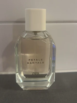 Zara Petale Santale parfym 100ml - Zara Petale Santale är en elegant parfym i en genomskinlig glasflaska med vit kork. Doften kommer i en stilren, sexkantig flaska som ger ett lyxigt intryck och passar perfekt på sminkbordet. Volymen är 100 ml.