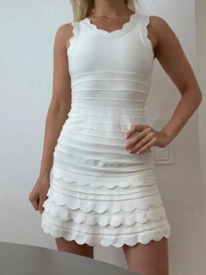 Vit klänning / studentklänning - Supersöt vit kort klänning med vågiga kanter och figurnära passform. Klänningen är ärmlös och har ett ribbat mönster med flera lager som ger en unik look. Perfekt till studenten!!