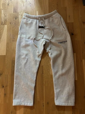 Gråa Essentials mjukisbyxor - Säljer ett par gråa mjukisbyxor från Fear of God Essentials. ”Fear of God” märket vid benet är lite borta men fortfarande synligt