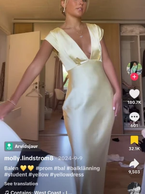 Gul långklänning från Saints & Secrets - Elegant gul långklänning från Saints & Secrets(Hello Molly)  i glansigt satinliknande material. Klänningen har djup v-ringning, korta ärmar och figurnära passform. Perfekt för bal eller student. Snygg och stilren design med lyxig känsla.