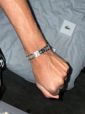 Silverfärgat armband från Lacoste - Snyggt armband i silverfärgad metall från Lacoste med klassisk krokodil-logga. Länkarna har en stilren, modern design och armbandet kommer med originalförpackning och tygpåse. Perfekt accessoar för dig som gillar en clean och sportig look.