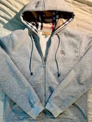 Grå zip hoodie från Burberry - Snygg grå zip hoodie från Burberry med klassiskt rutigt foder i huvan och dragsko. Diskret Burberry-logga broderad på bröstet. Tillverkad i mjuk bomullsblandning, perfekt för en chill och stilren look. Nytt skick . S men passar XS utmärkt.