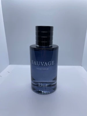 Dior Sauvage Eau de Parfum - Dior Sauvage Eau de Parfum i en elegant cylinderformad glasflaska med mörkblå toning och svart lock. Flaskan har silverfärgade detaljer och tydlig logga. En ikonisk doft som utstrålar modern maskulinitet och stil.